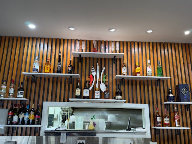 Bar shelves with spirits and cutlery wall art against timber slat panelling